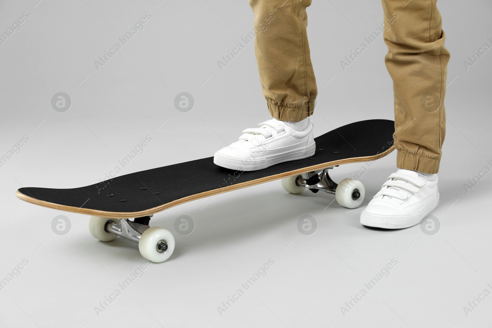 Photo of Little boy with skateboard on light grey background, closeup