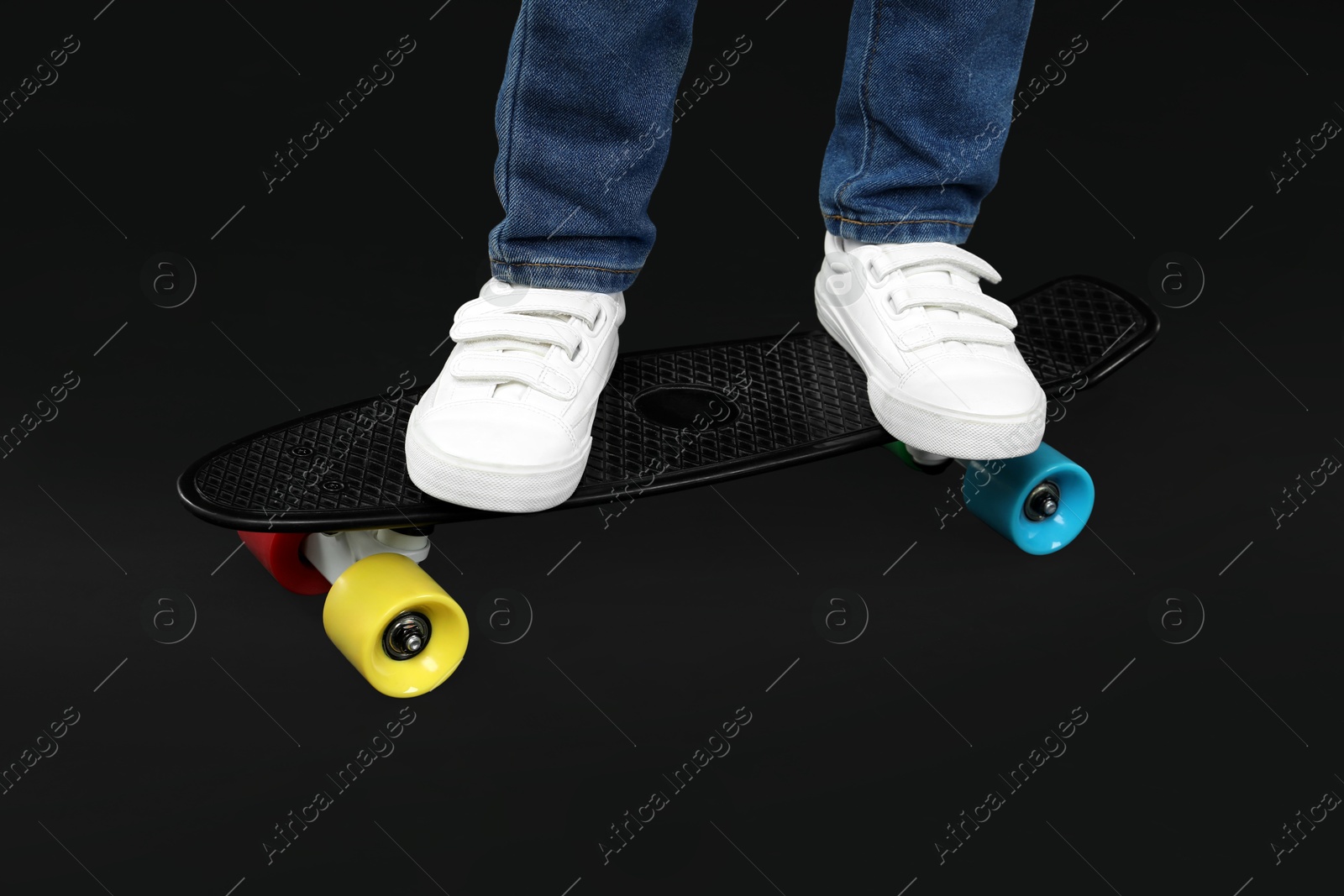 Photo of Little boy with skateboard on black background, closeup