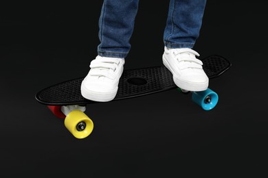 Little boy with skateboard on black background, closeup