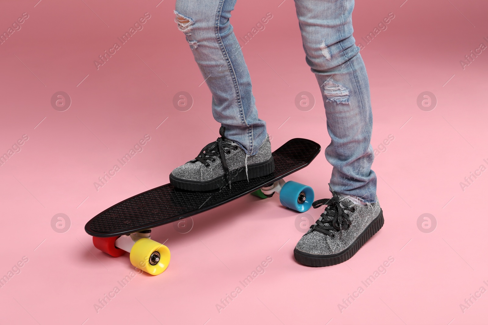 Photo of Little girl with penny board on pink background, closeup