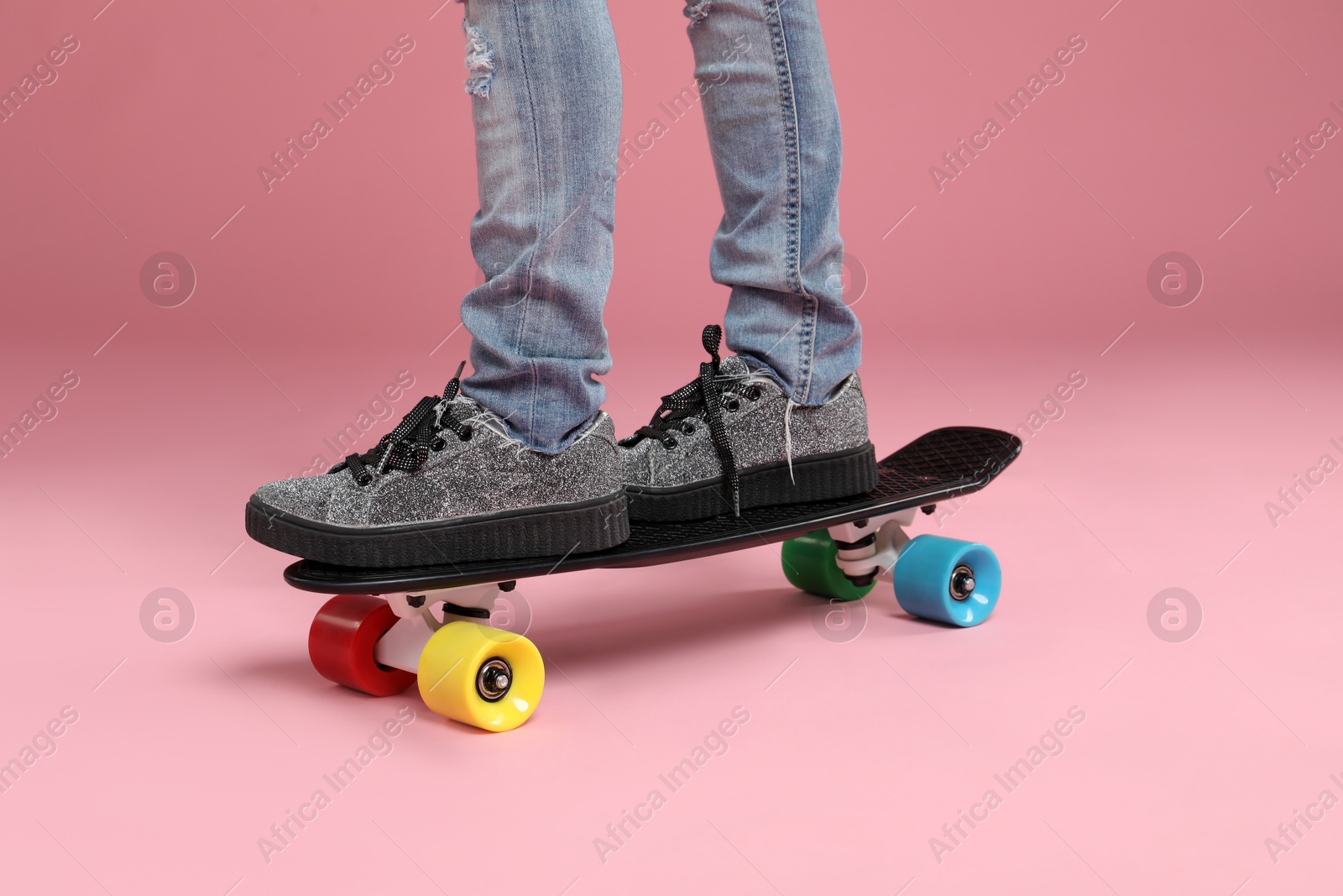 Photo of Little girl standing on penny board against pink background, closeup