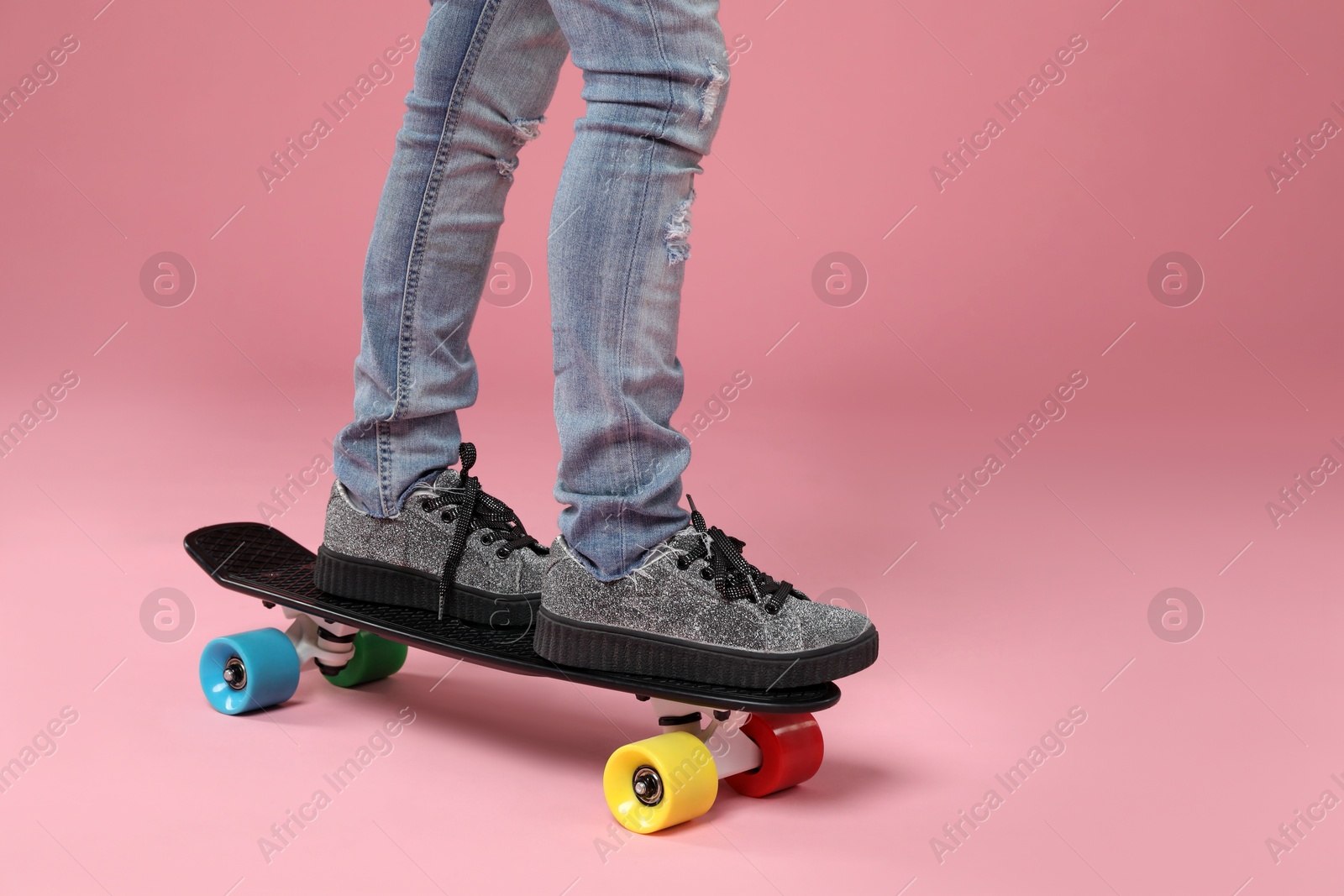 Photo of Little girl standing on penny board against pink background, closeup. Space for text