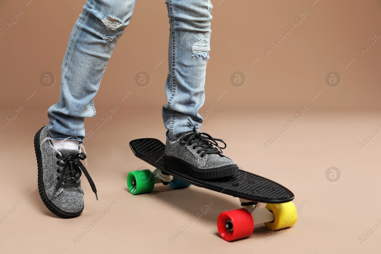 Photo of Little girl with penny board on pale brown background, closeup