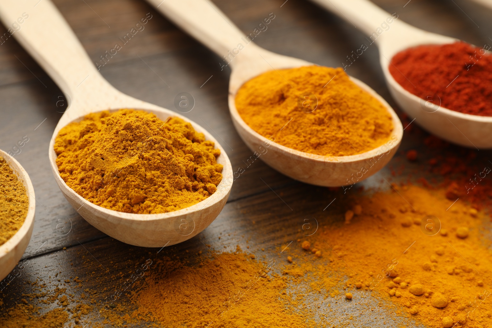 Photo of Different aromatic spices in spoons on wooden table, closeup