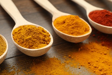 Photo of Different aromatic spices in spoons on wooden table, closeup