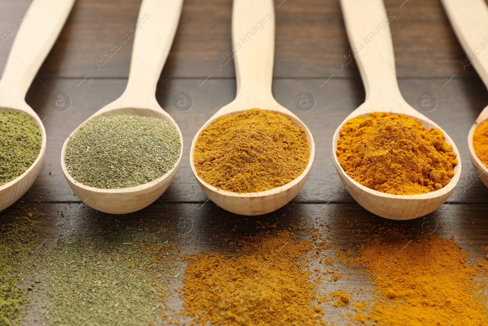 Photo of Different aromatic spices in spoons on wooden table, closeup