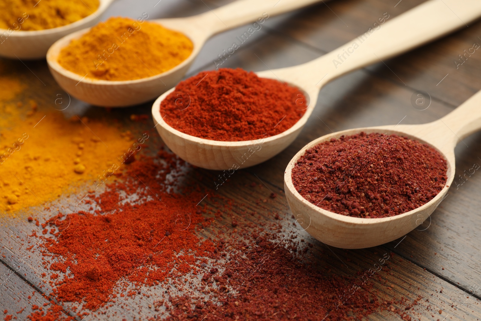 Photo of Different aromatic spices in spoons on wooden table, closeup