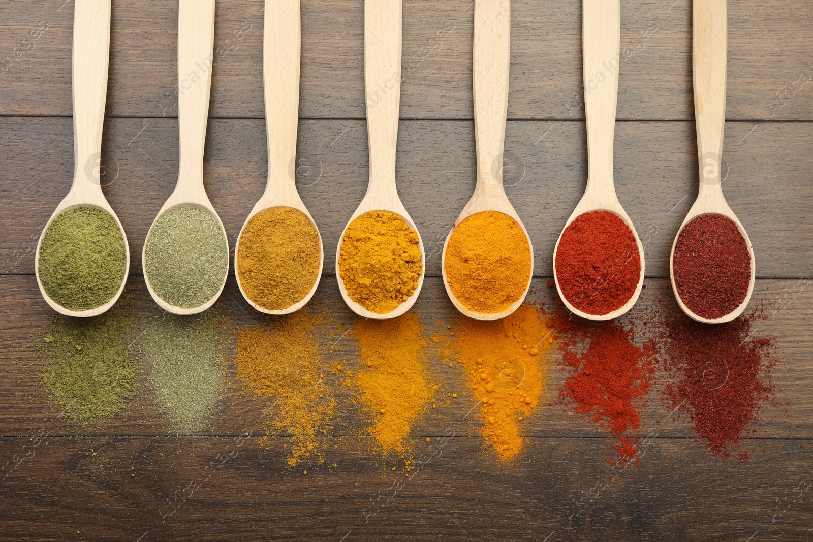 Photo of Different aromatic spices in spoons on wooden table, flat lay