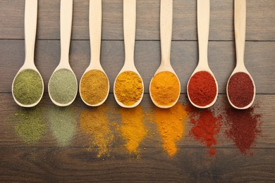 Different aromatic spices in spoons on wooden table, flat lay