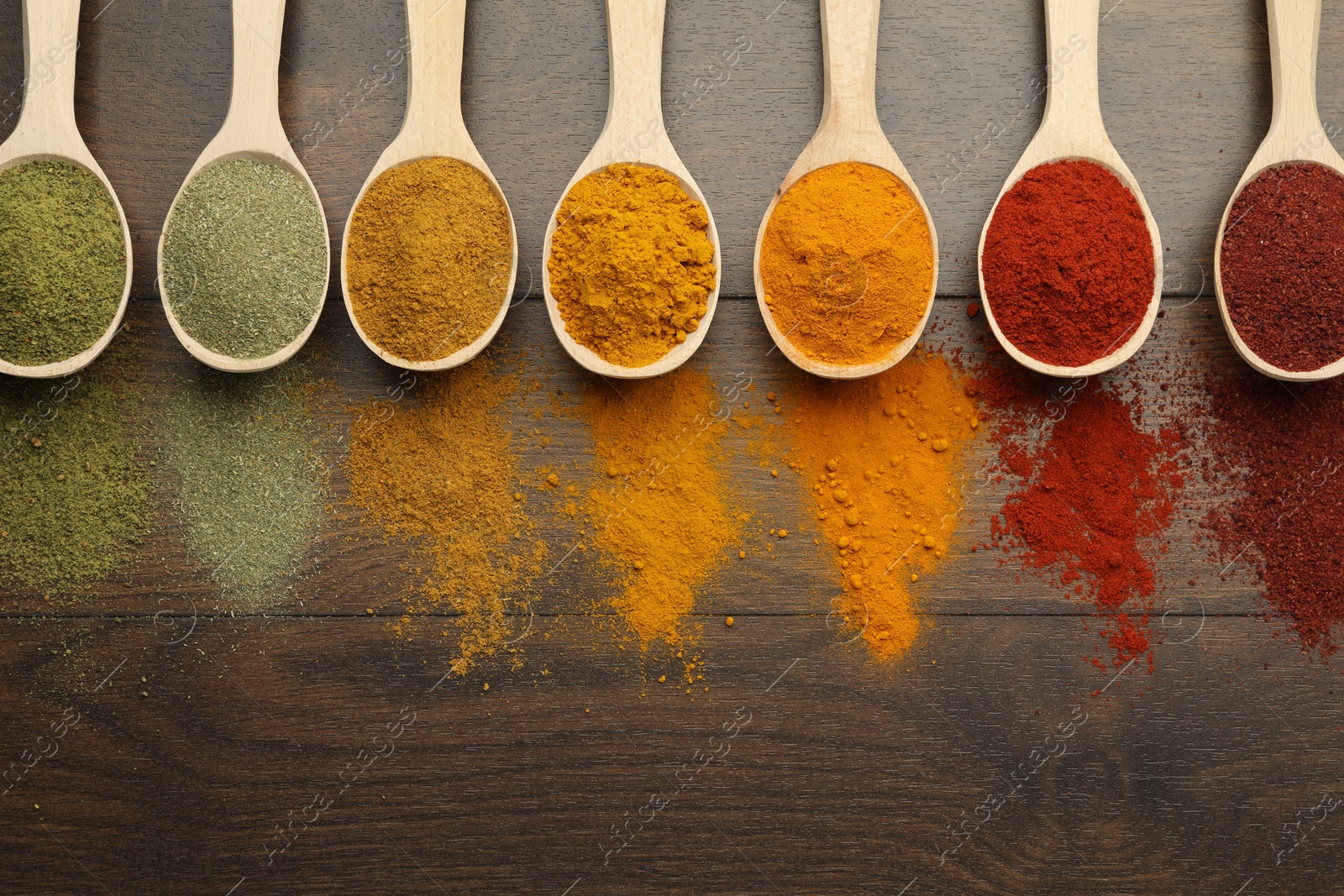 Photo of Different aromatic spices in spoons on wooden table, flat lay. Space for text