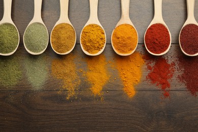 Photo of Different aromatic spices in spoons on wooden table, flat lay. Space for text