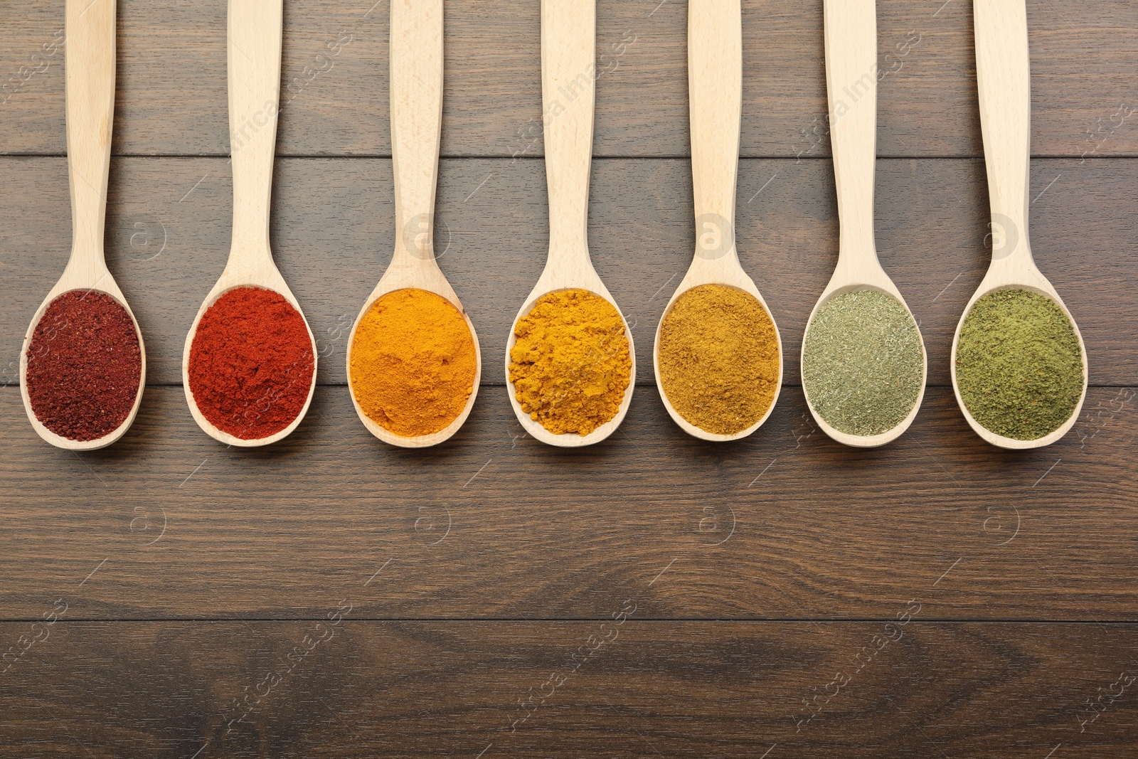 Photo of Different aromatic spices in spoons on wooden table, flat lay. Space for text