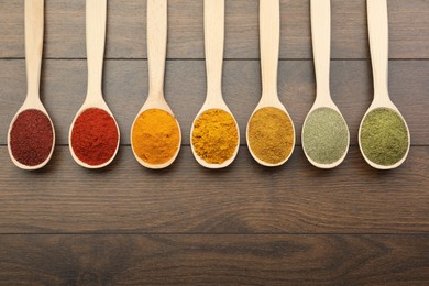 Different aromatic spices in spoons on wooden table, flat lay. Space for text