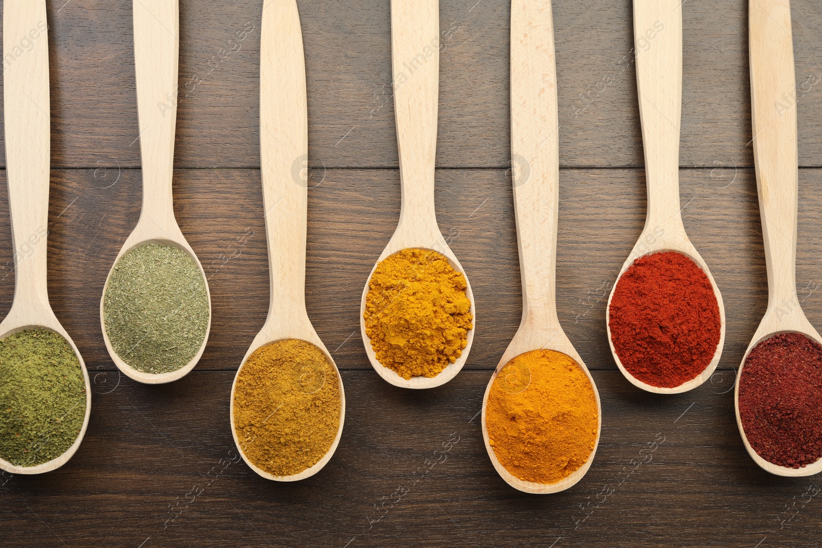 Photo of Different aromatic spices in spoons on wooden table, flat lay