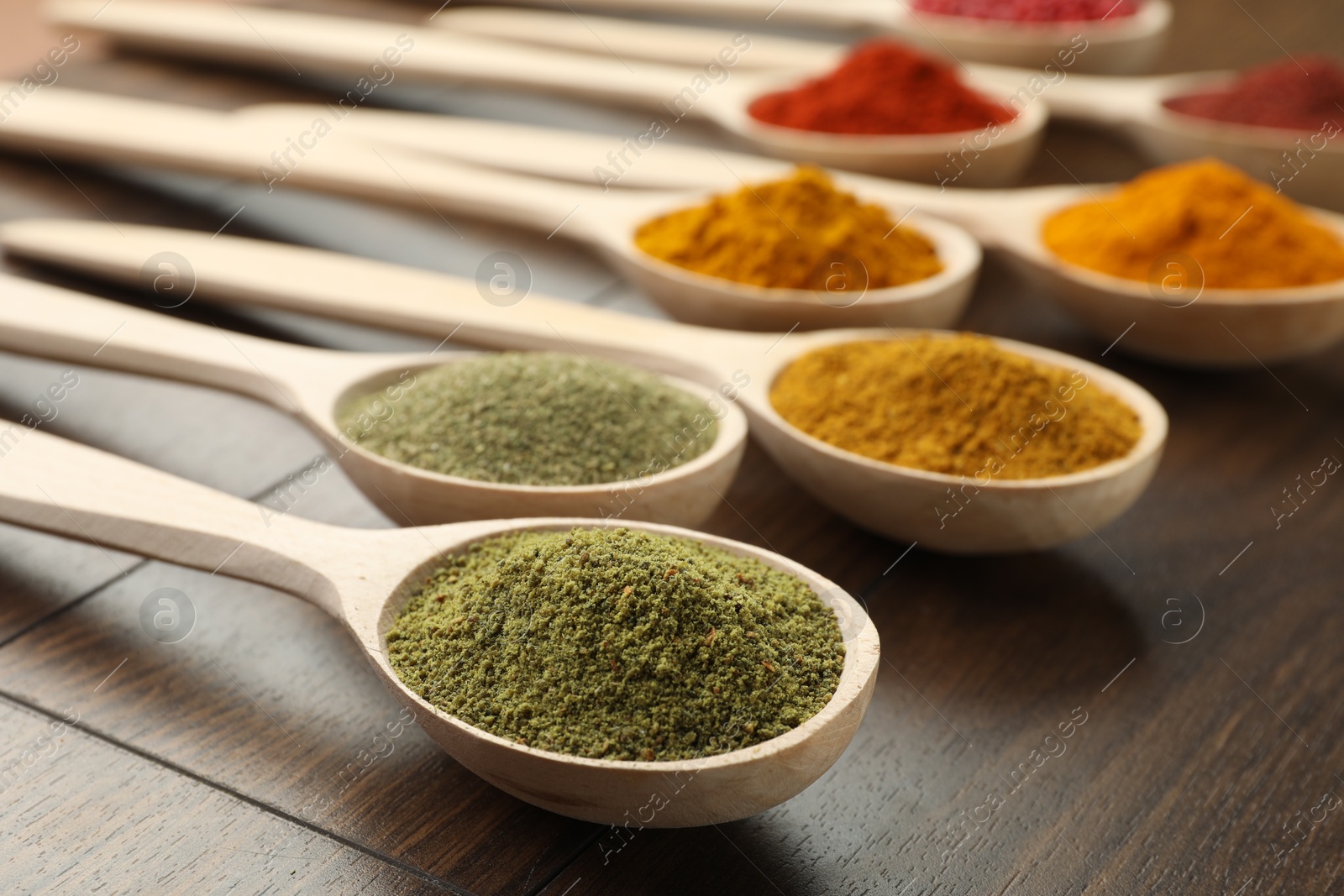 Photo of Different aromatic spices in spoons on wooden table, closeup