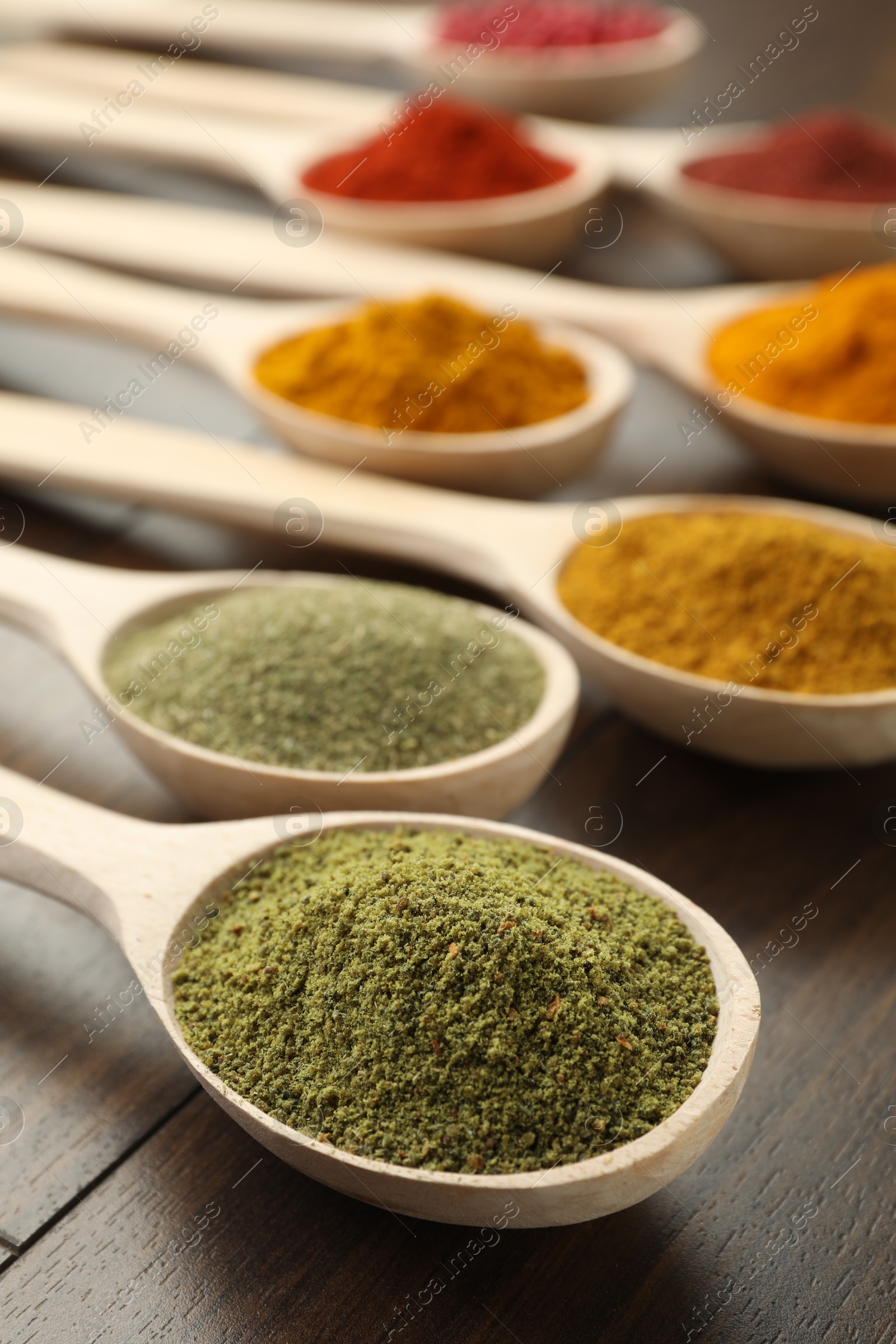 Photo of Different aromatic spices in spoons on wooden table, closeup