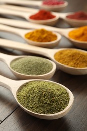 Photo of Different aromatic spices in spoons on wooden table, closeup