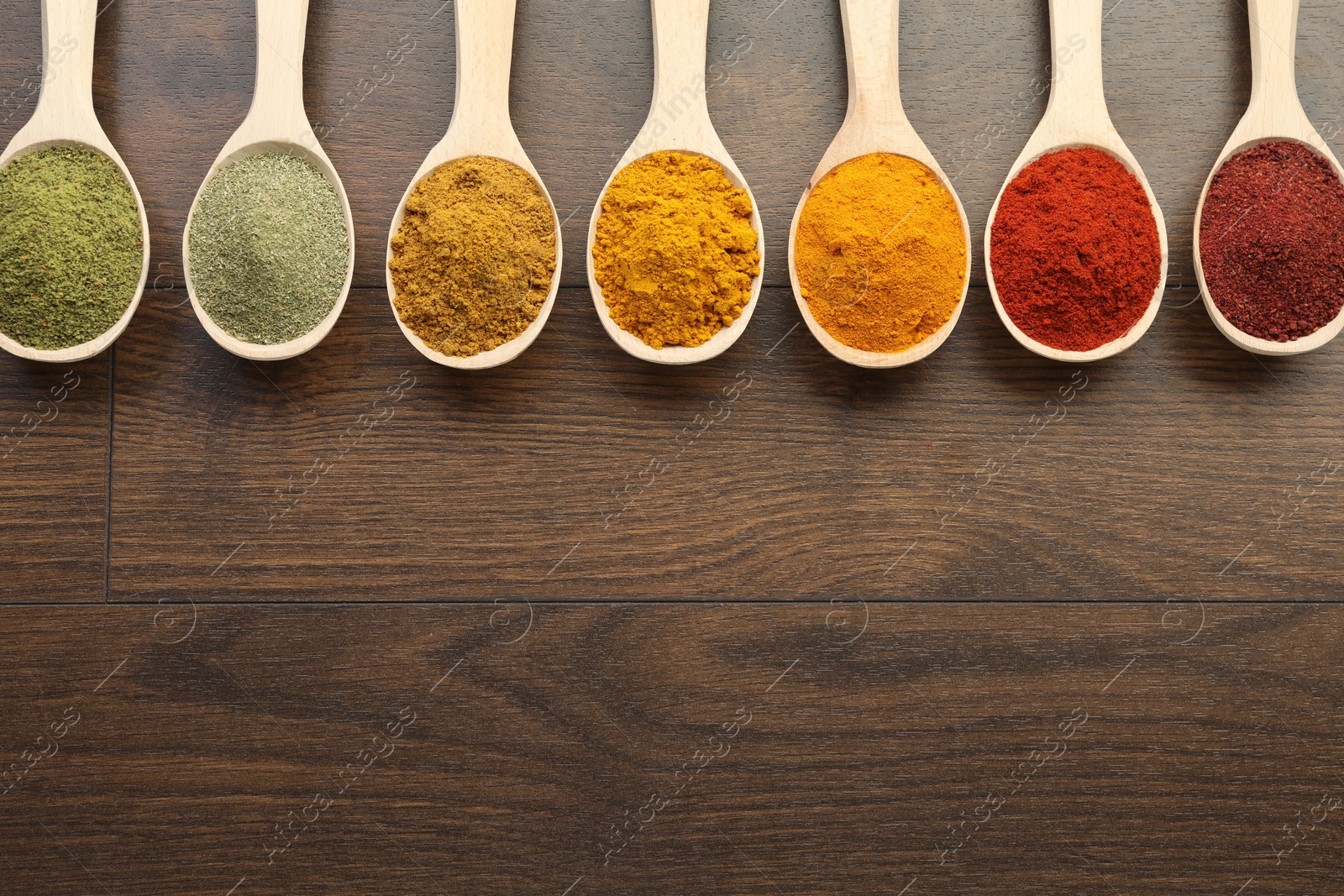 Photo of Different aromatic spices in spoons on wooden table, flat lay. Space for text