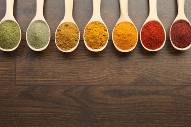 Photo of Different aromatic spices in spoons on wooden table, flat lay. Space for text