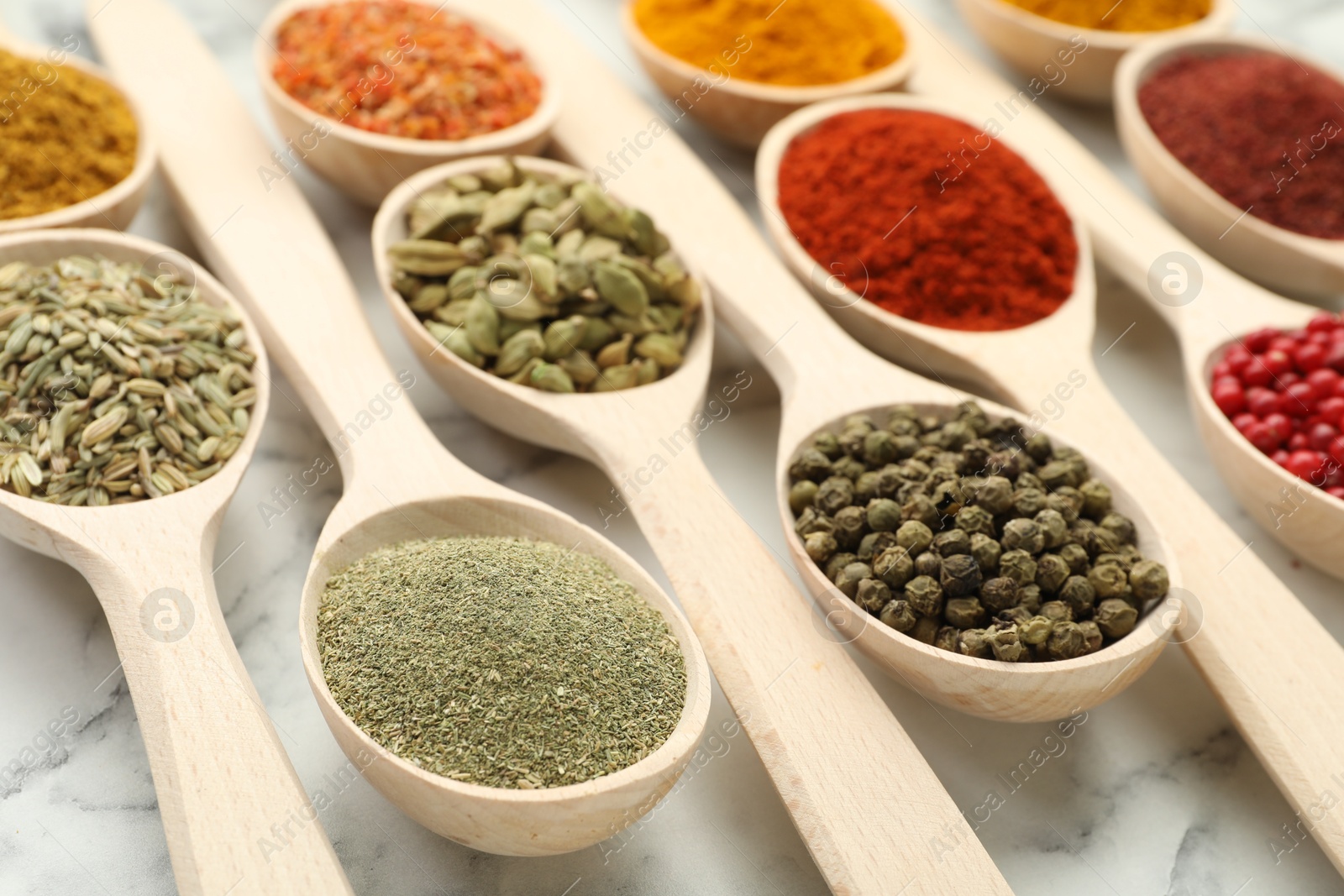 Photo of Different aromatic spices in spoons on white marble table, closeup