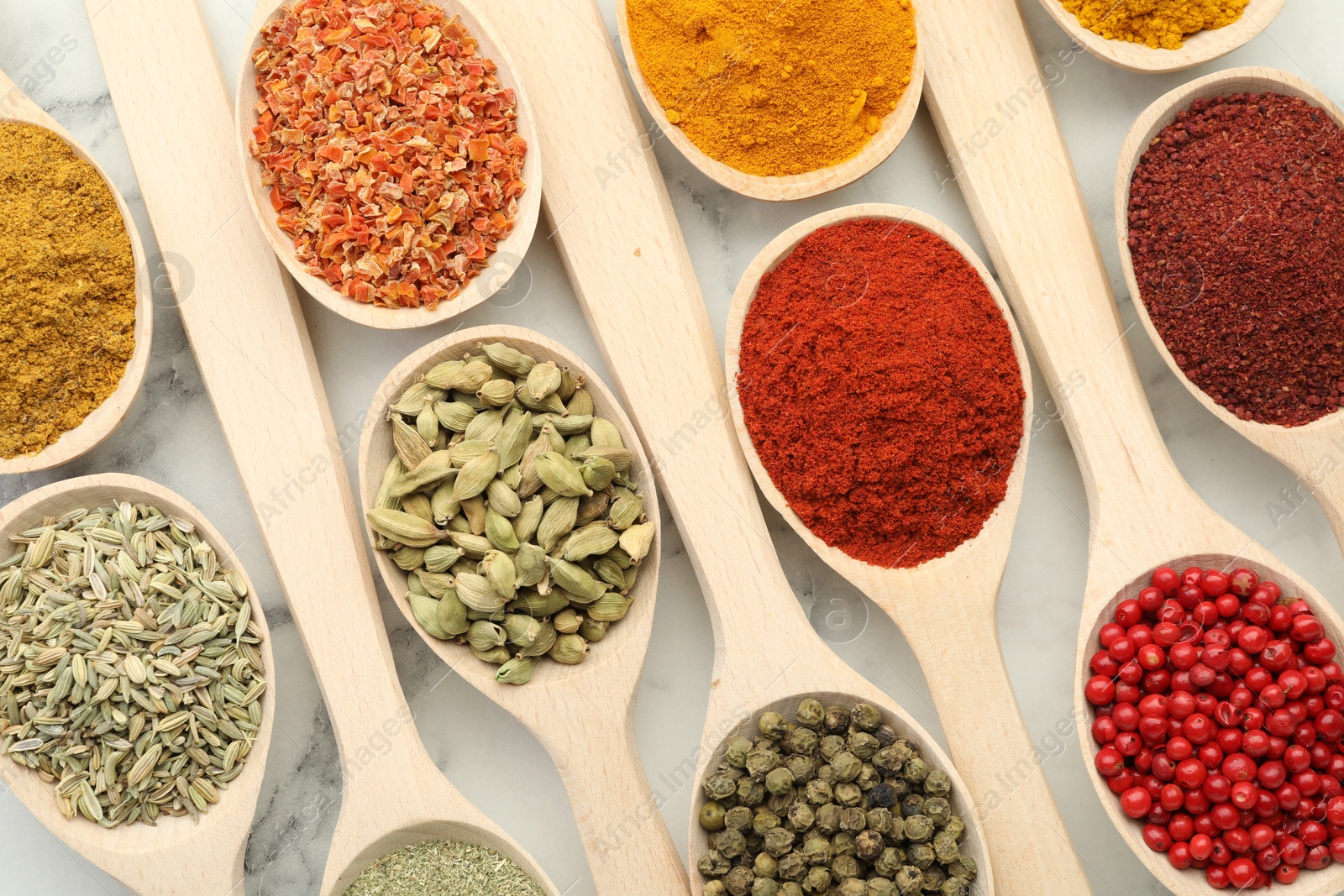 Photo of Different aromatic spices in spoons on white marble table, flat lay