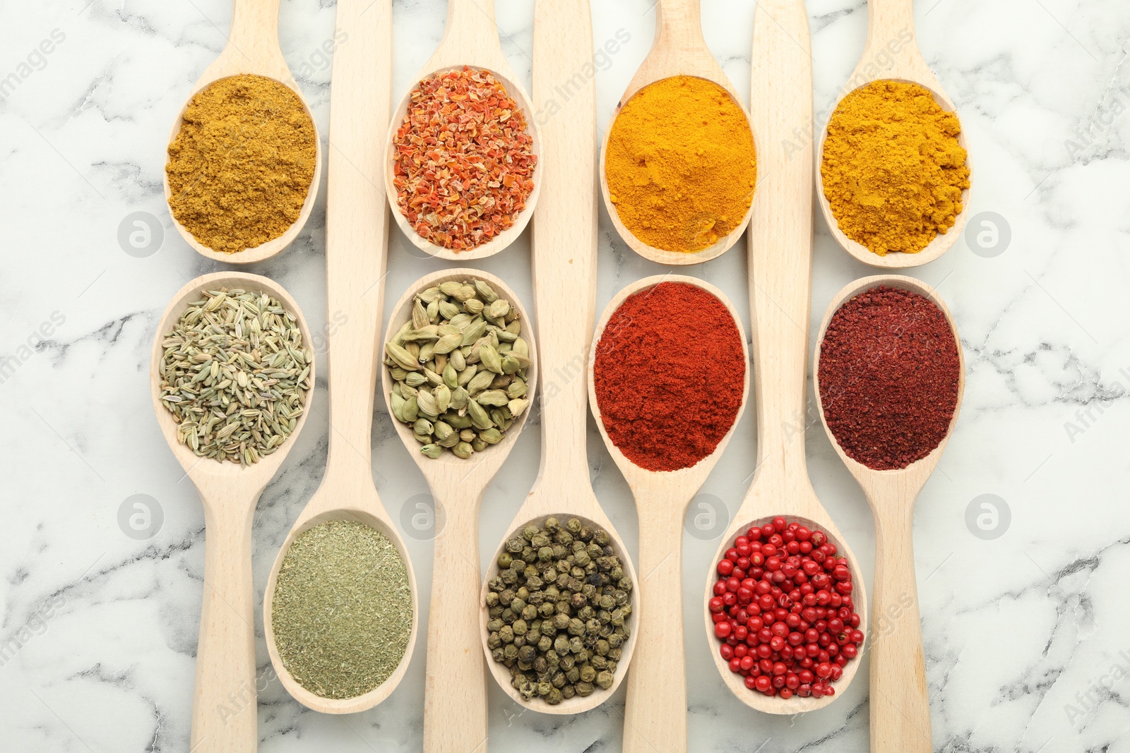 Photo of Different aromatic spices in spoons on white marble table, flat lay