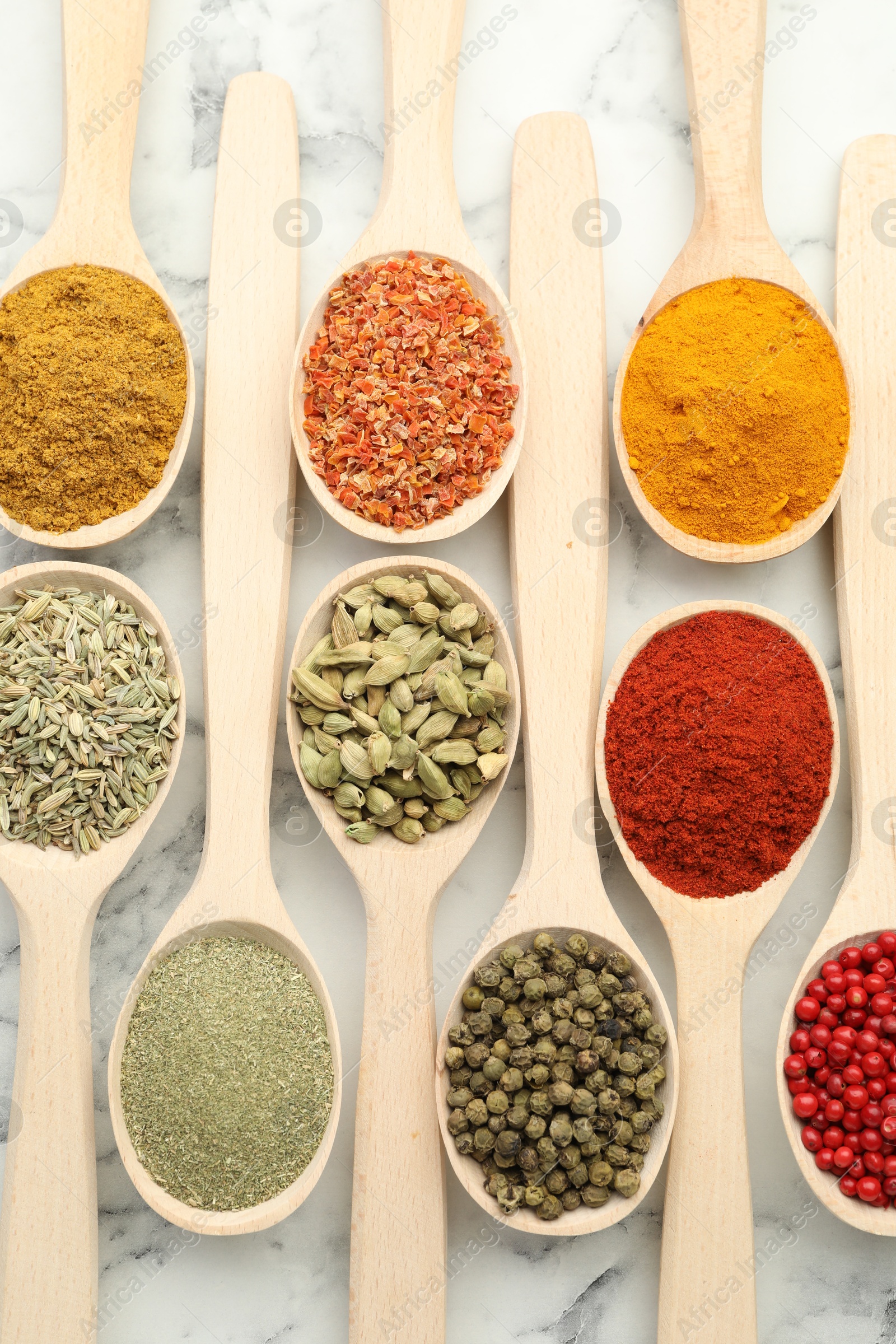 Photo of Different aromatic spices in spoons on white marble table, flat lay