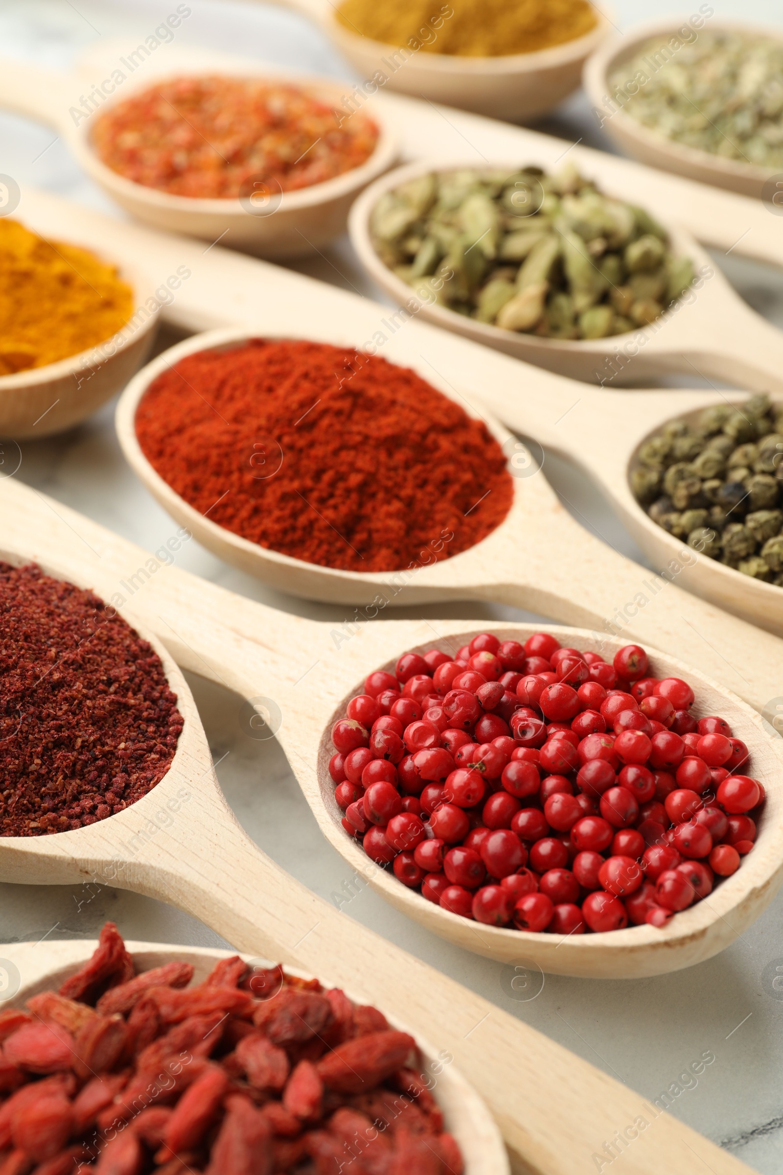 Photo of Different aromatic spices in spoons on white marble table, closeup