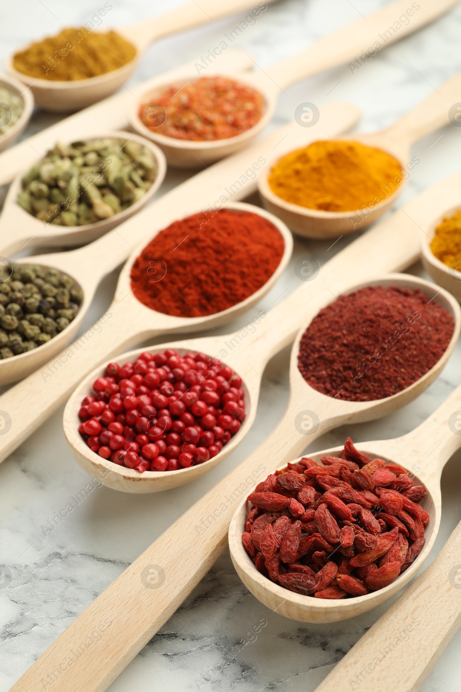 Photo of Different aromatic spices in spoons on white marble table, closeup