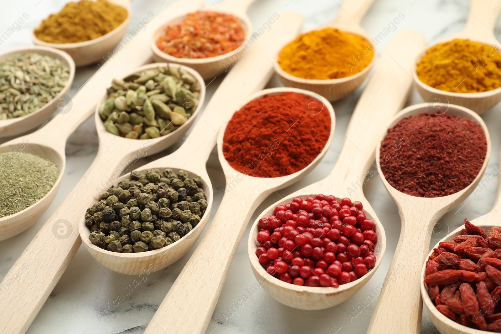 Photo of Different aromatic spices in spoons on white marble table, closeup