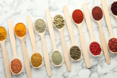 Photo of Different aromatic spices in spoons on white marble table, flat lay