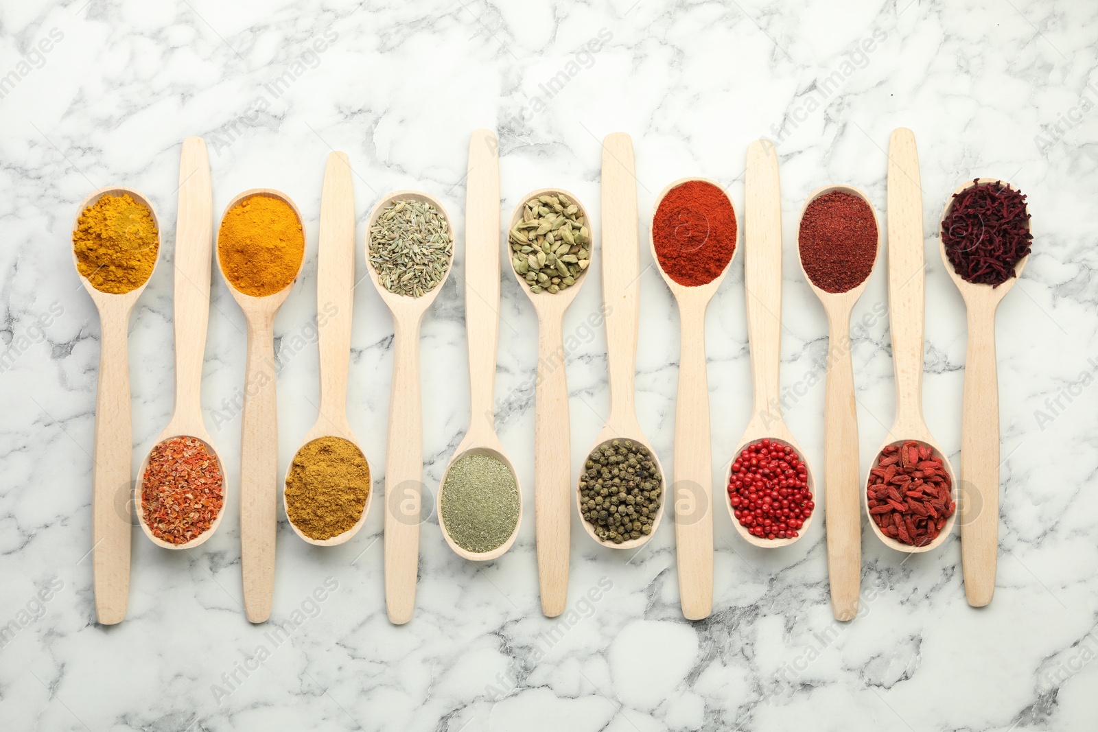 Photo of Different aromatic spices in spoons on white marble table, flat lay