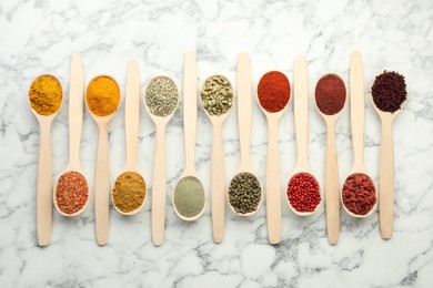 Different aromatic spices in spoons on white marble table, flat lay