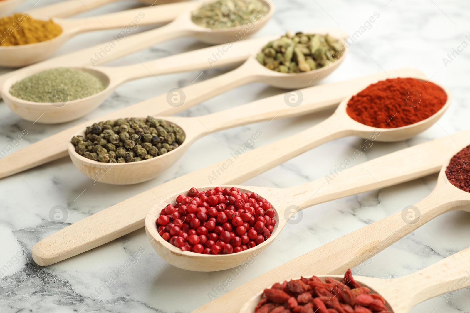 Photo of Different aromatic spices in spoons on white marble table, closeup