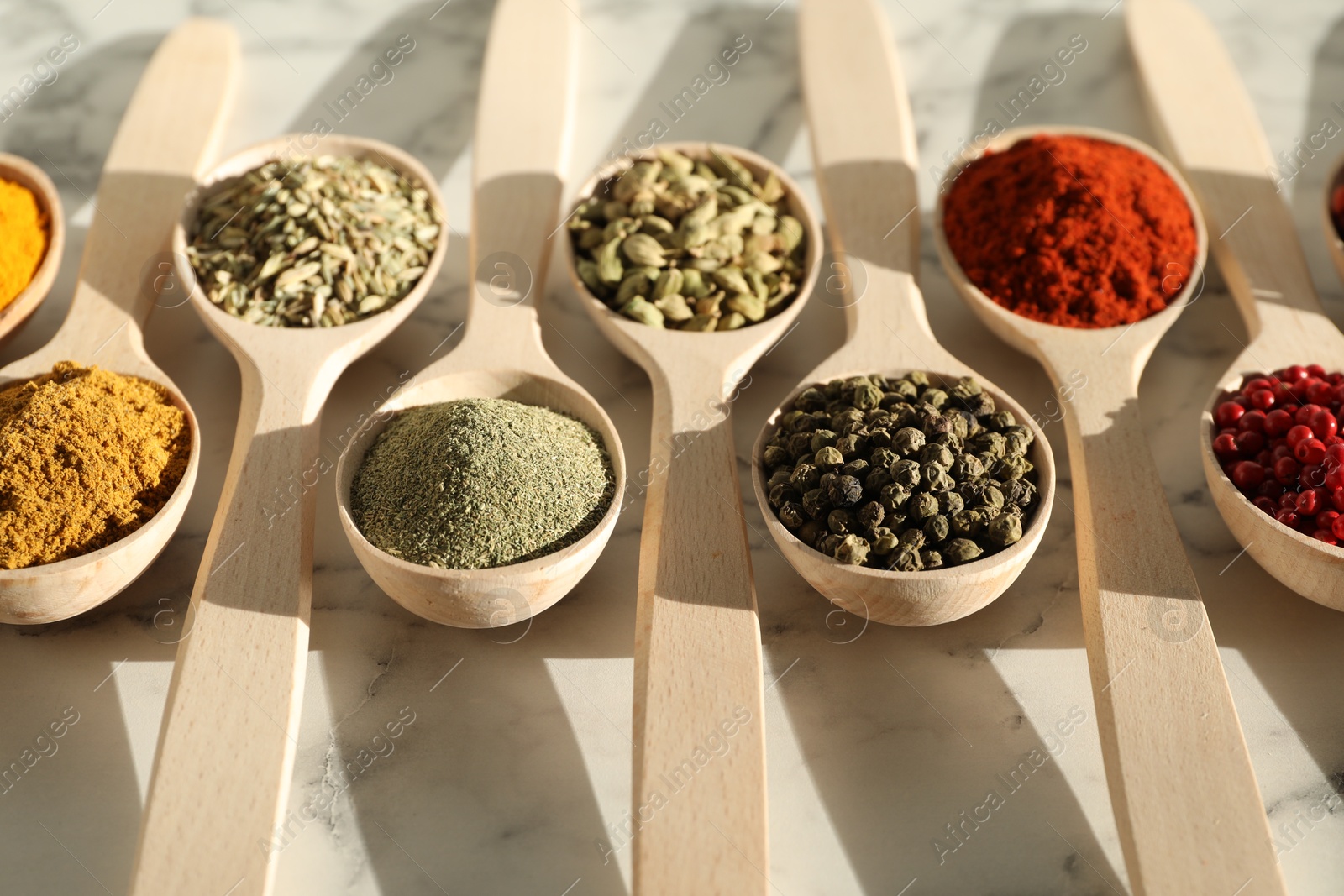 Photo of Different aromatic spices in spoons on white marble table, closeup