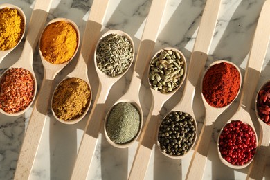 Photo of Different aromatic spices in spoons on white marble table, flat lay