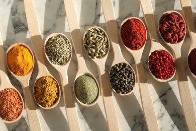 Photo of Different aromatic spices in spoons on white marble table, flat lay