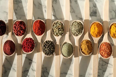 Photo of Different aromatic spices in spoons on white marble table, flat lay