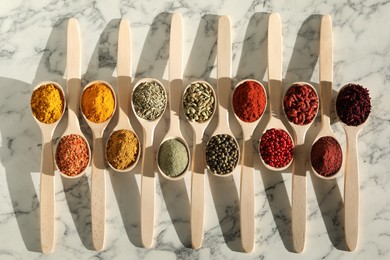 Photo of Different aromatic spices in spoons on white marble table, flat lay