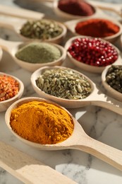 Photo of Different aromatic spices in spoons on white marble table, closeup