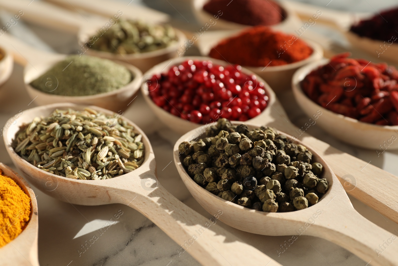 Photo of Different aromatic spices in spoons on white marble table, closeup