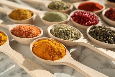 Photo of Different aromatic spices in spoons on white marble table, closeup