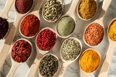 Different aromatic spices in spoons on white marble table, flat lay