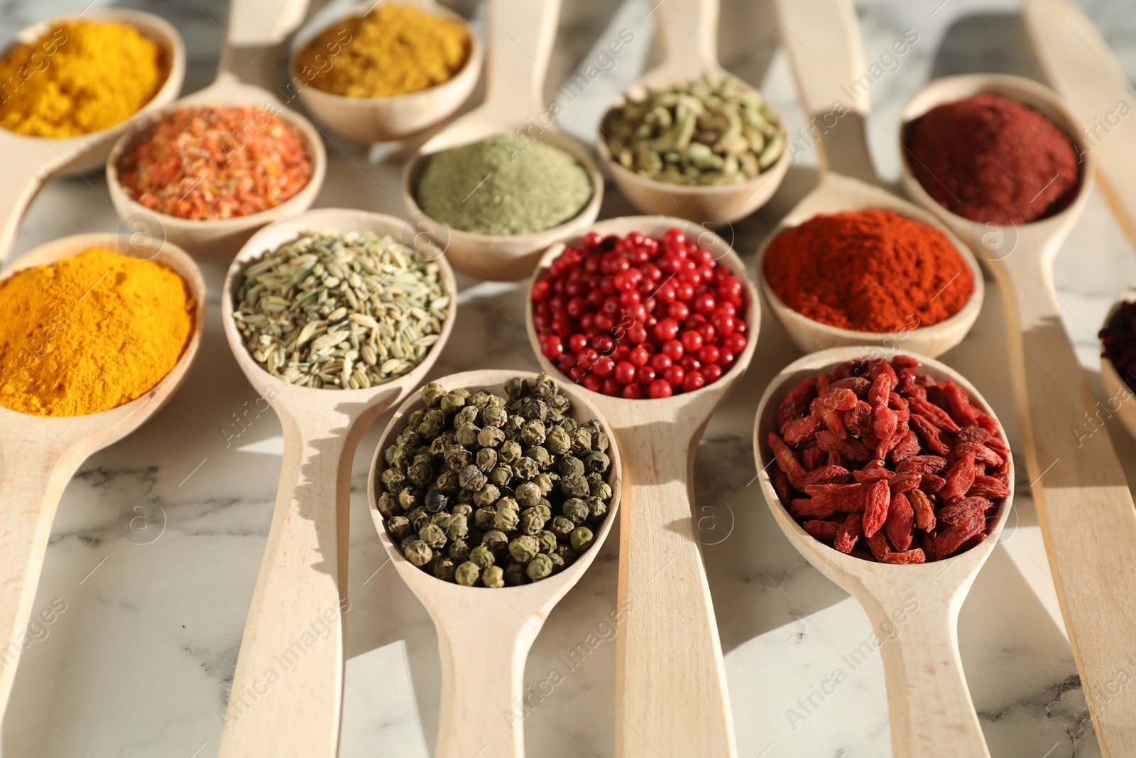 Photo of Different aromatic spices in spoons on white marble table, closeup