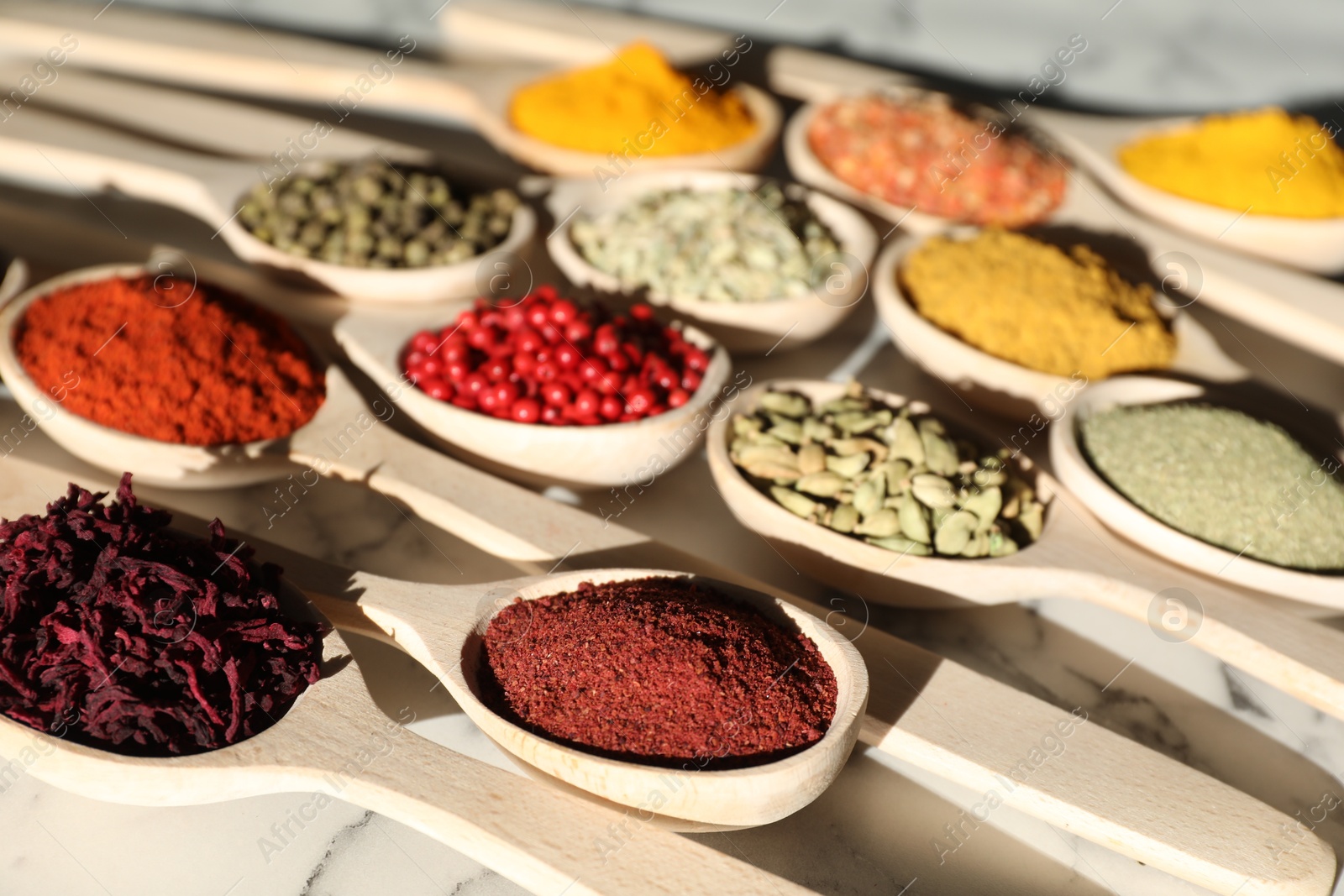 Photo of Different aromatic spices in spoons on white marble table, closeup