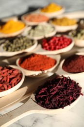 Photo of Different aromatic spices in spoons on white marble table, closeup