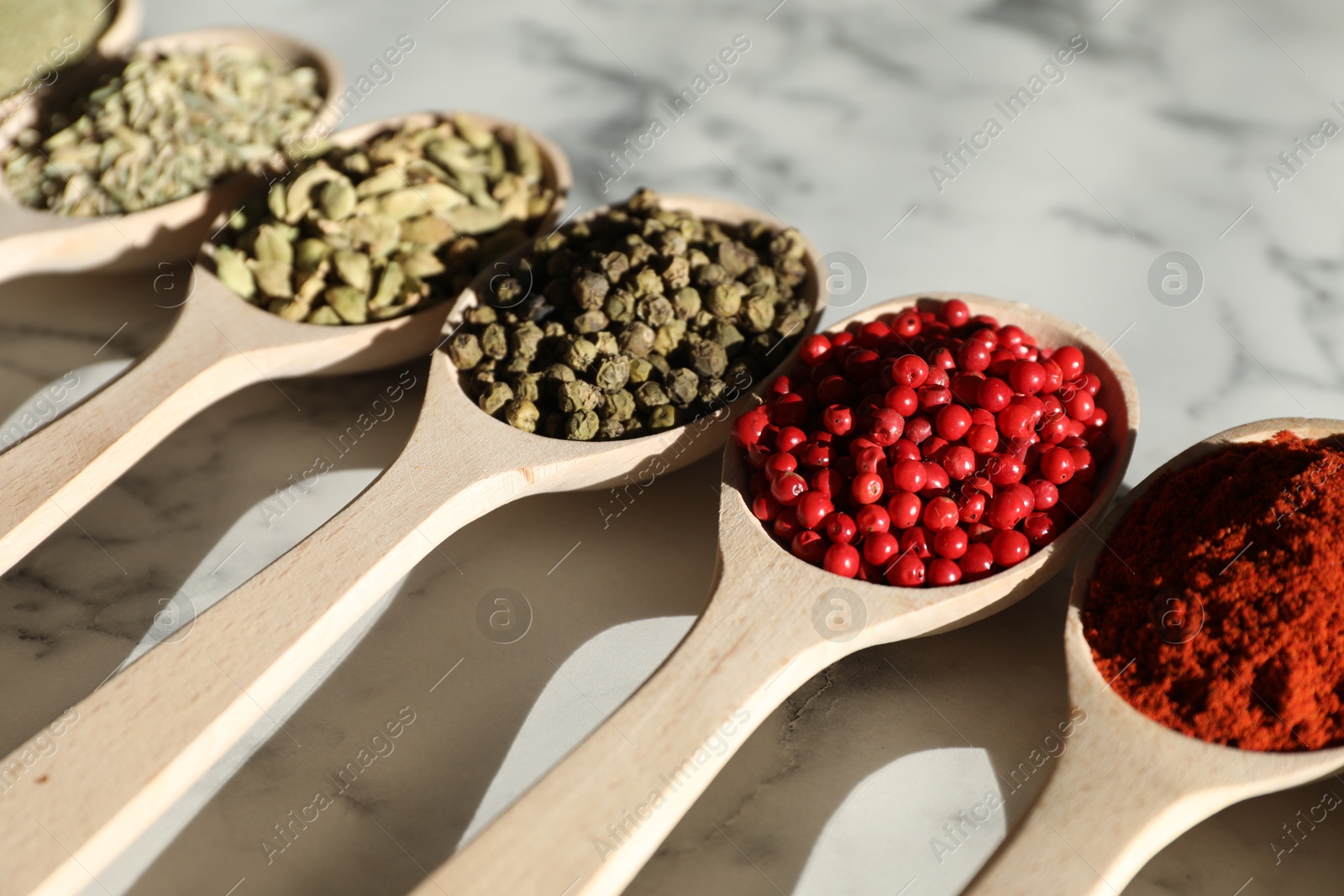 Photo of Different aromatic spices in spoons on white marble table, closeup