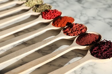 Photo of Different aromatic spices in spoons on white marble table, closeup