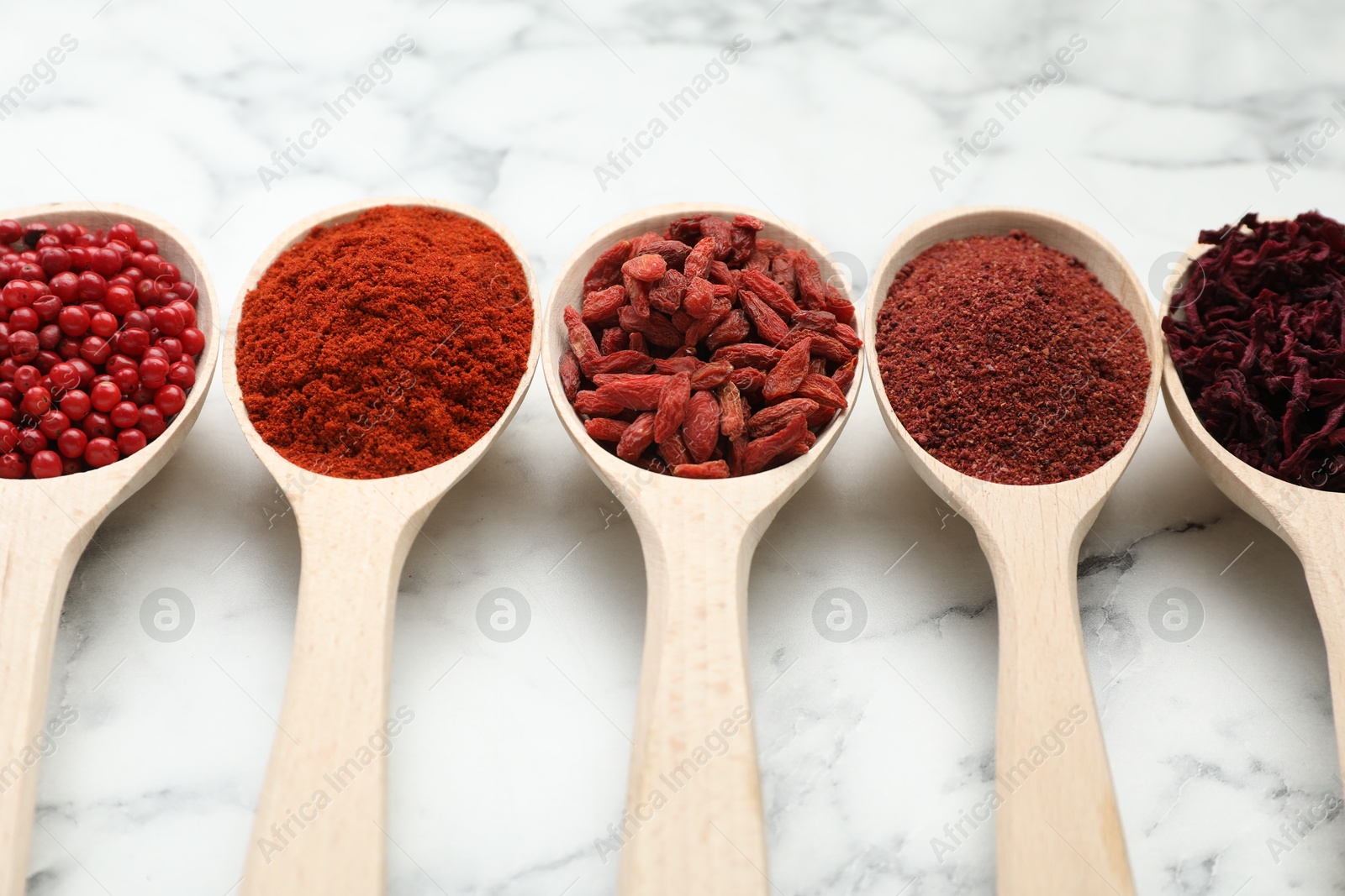 Photo of Different aromatic spices in spoons on white marble table, closeup