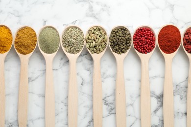 Photo of Different aromatic spices in spoons on white marble table, flat lay